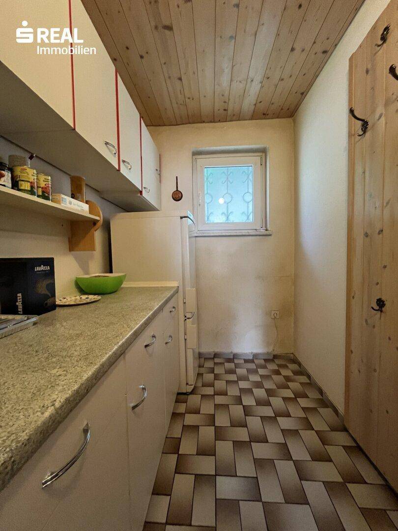 Kleine Küchenzeile mit Spüle, Kühlschrank und Holzdecke, ideal für einfache Mahlzeiten.