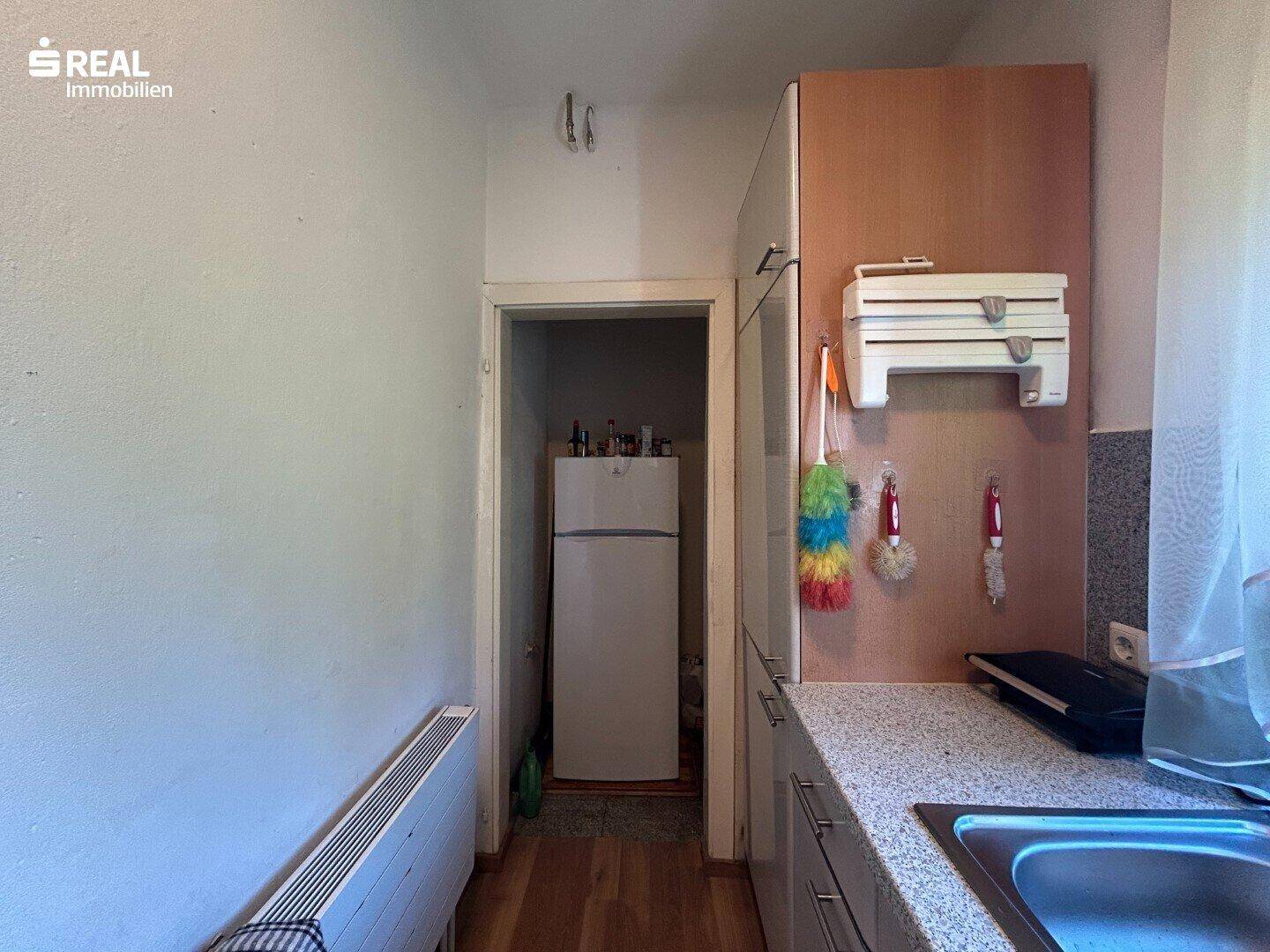 Küchenzeile mit Kühlschrank und Stauraum, die in einen weiteren Raum führt.