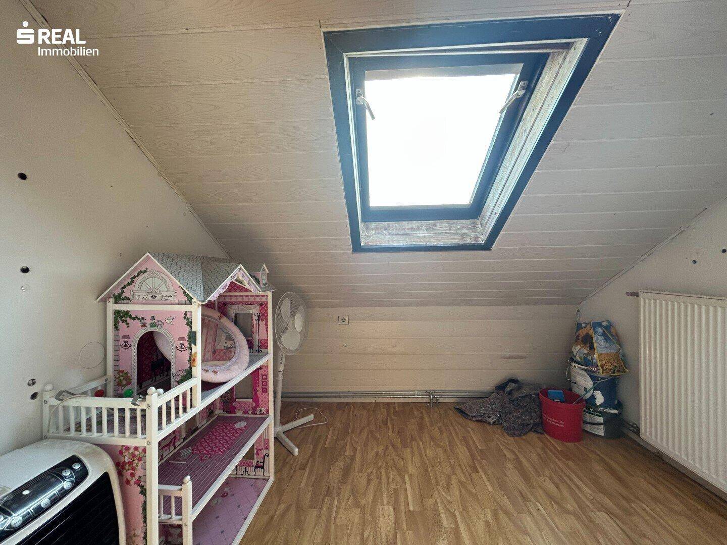 Dachgeschossraum als Spielbereich mit Dachfenster, Spielhaus und Laminatboden.
