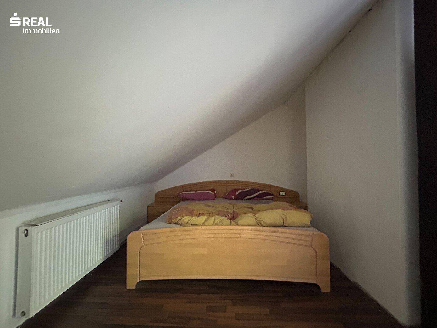 Schlafzimmer im Dachgeschoss mit Holzbett, Heizung und Laminatboden unter der Dachschräge.