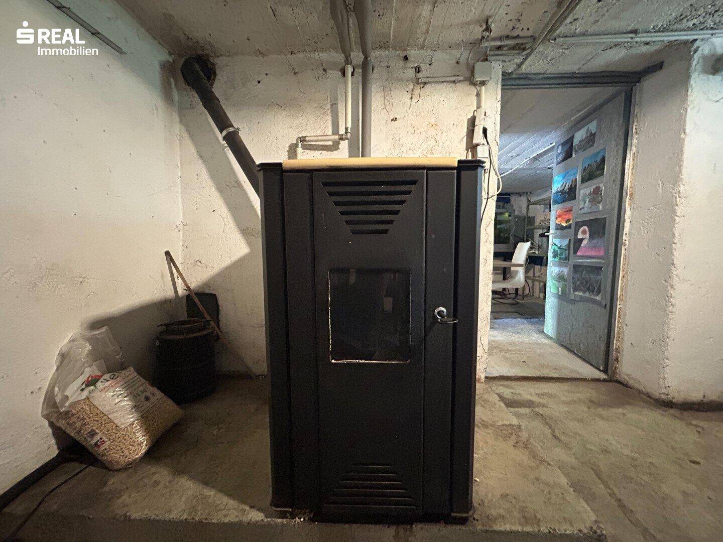 Heizungsraum im Keller mit einem Pelletsofen und sichtbaren Rohren an den Betonwänden.