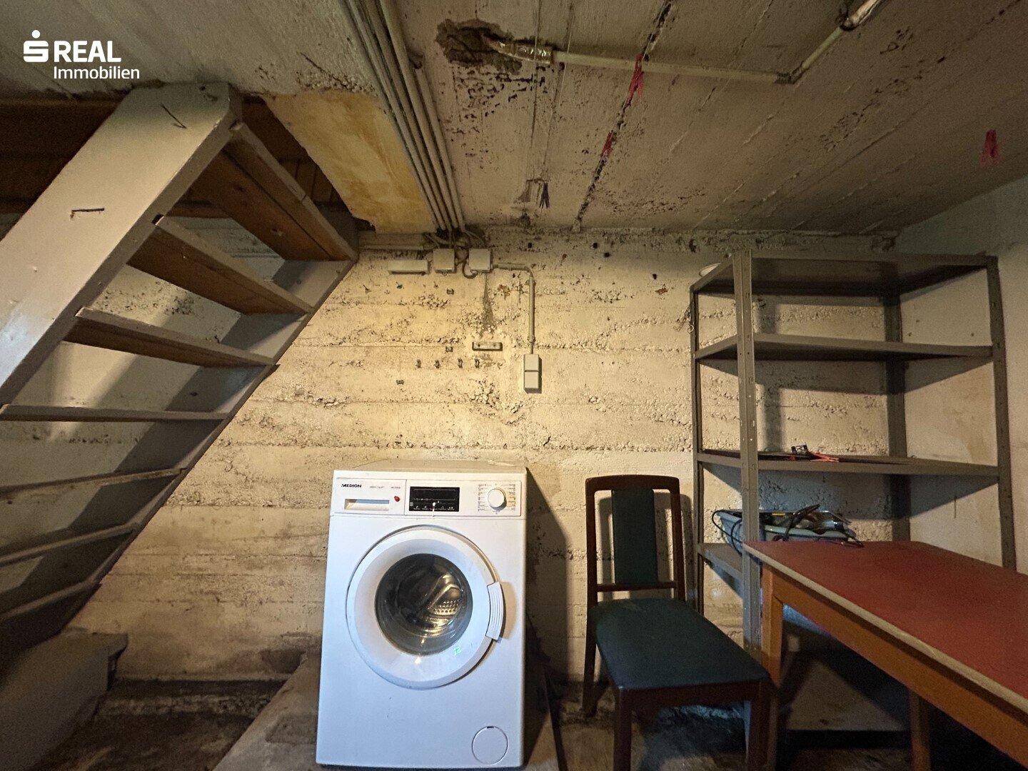 Waschküche im Keller mit Waschmaschine, Holztreppe und Lagerregalen für zusätzlichen Stauraum.