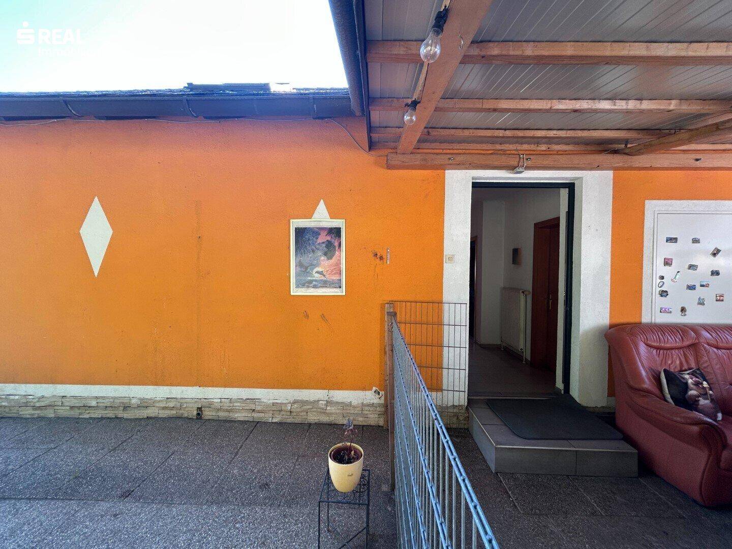 Detailansicht der überdachten Terrasse mit einfacher Einrichtung und Zugang zum Haus.