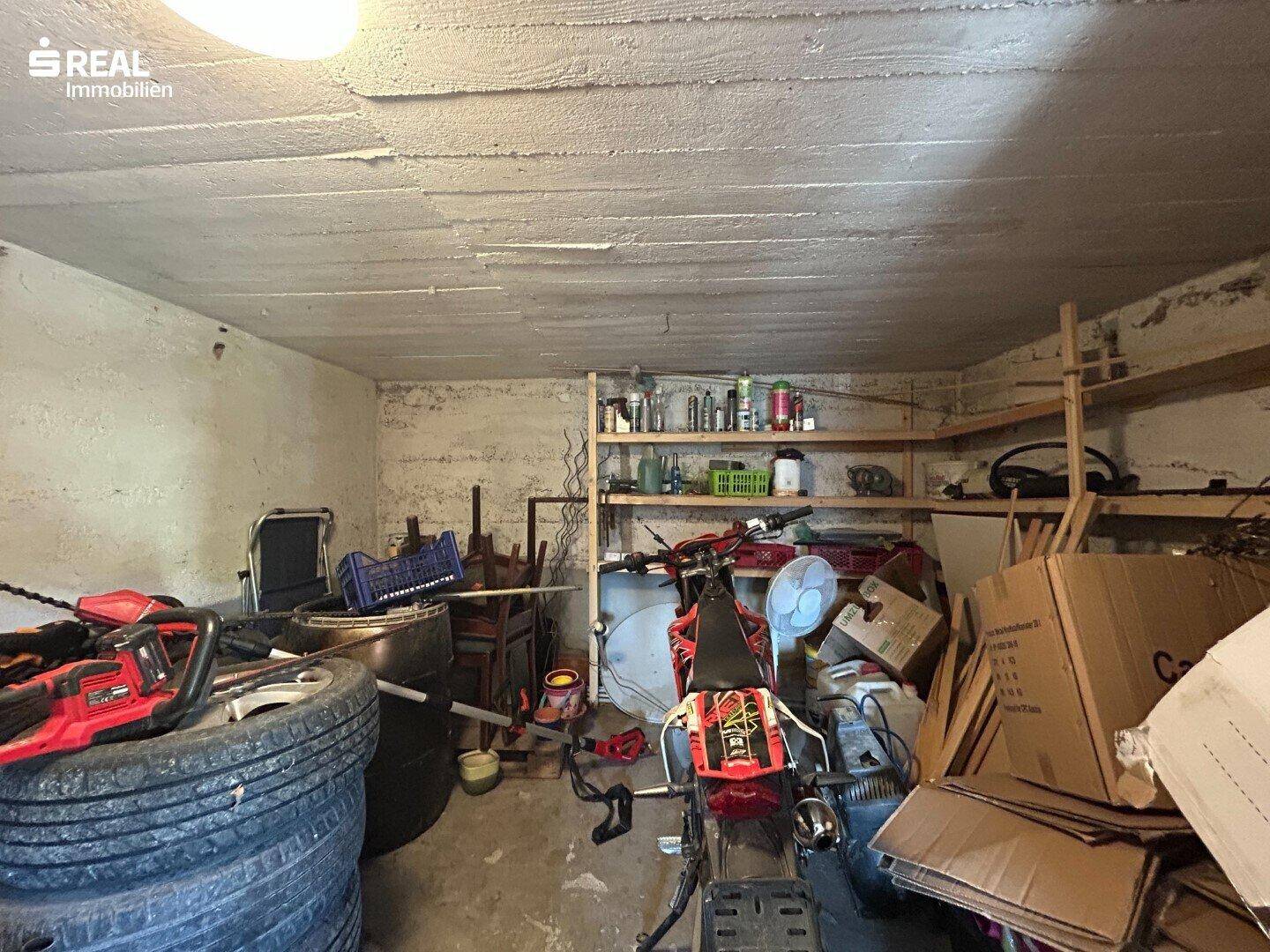 Unaufgeräumter Kellerraum mit Reifen, einem Motorrad, Regalen und vielen Kartons.
