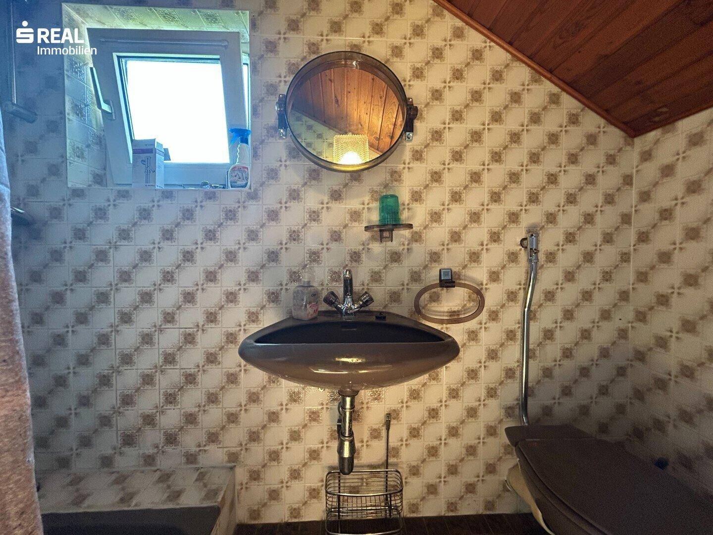 Badezimmer im Dachgeschoss mit Waschbecken, WC und gemusterten Fliesen.