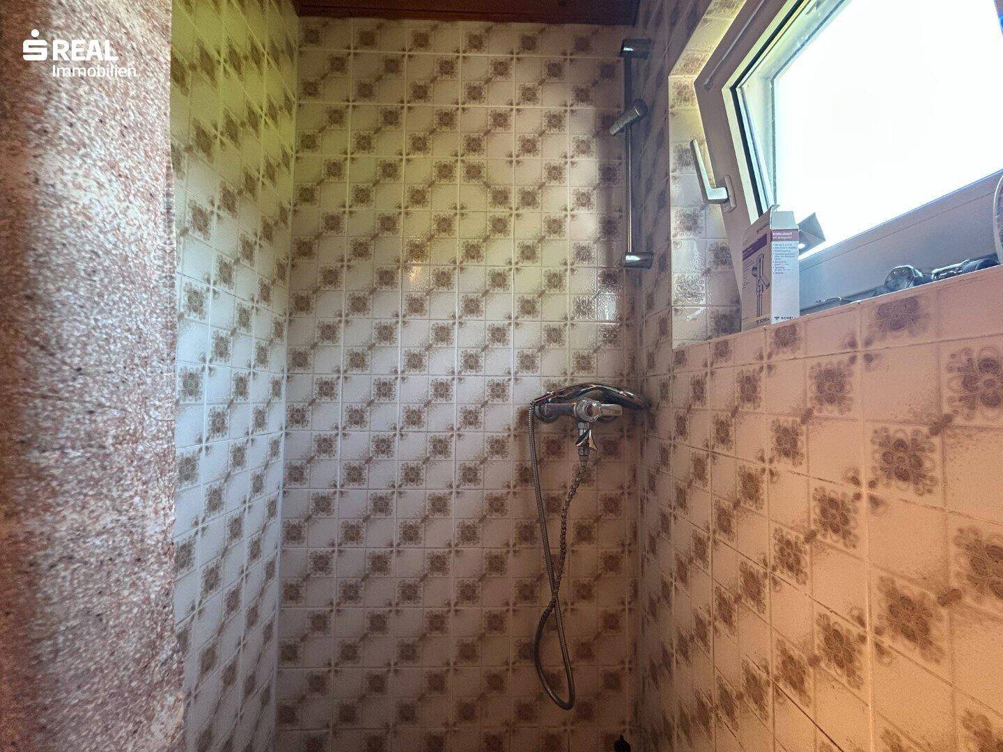 Duschbereich im Dachgeschoss mit gemusterten Fliesen und Fenster.