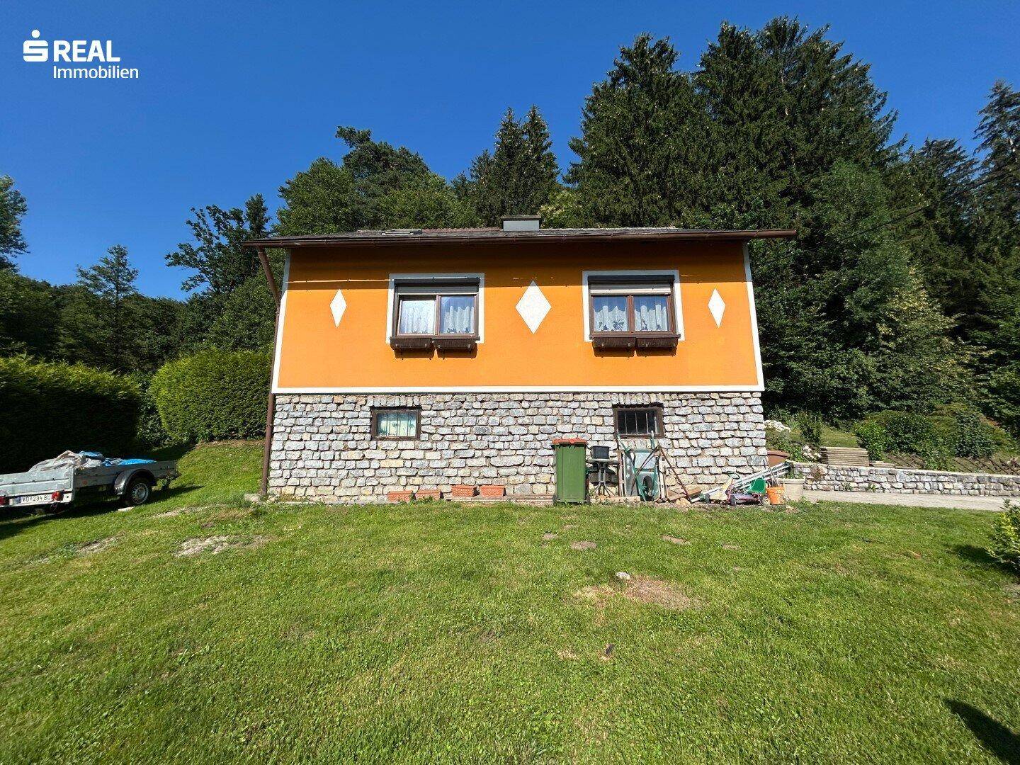 Seitenansicht des Hauses mit orangefarbener Fassade, Steinsockel und großem Rasenbereich.