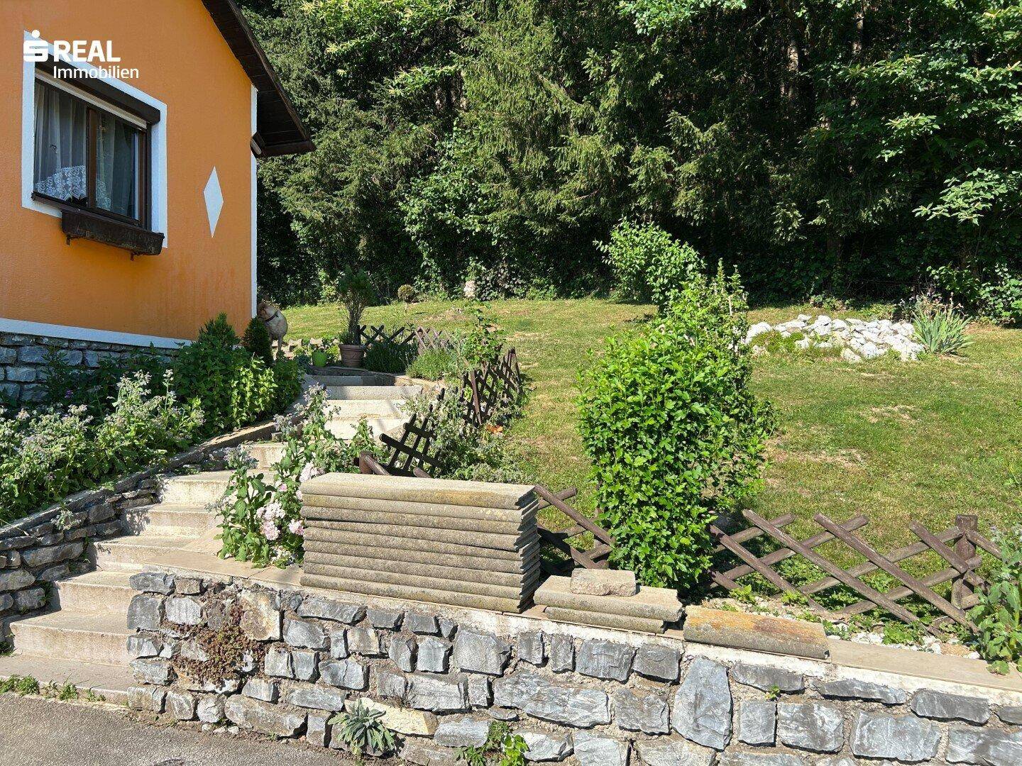Steintreppe und Gartenbereich mit üppigem Grün, die zum Haus hinaufführen.