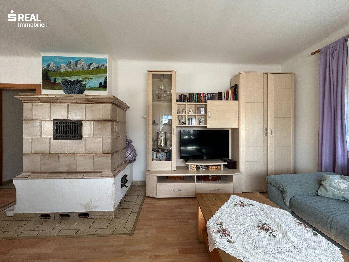 Wohnbereich mit traditionellem Kachelofen, Medienschrank und Holzboden.