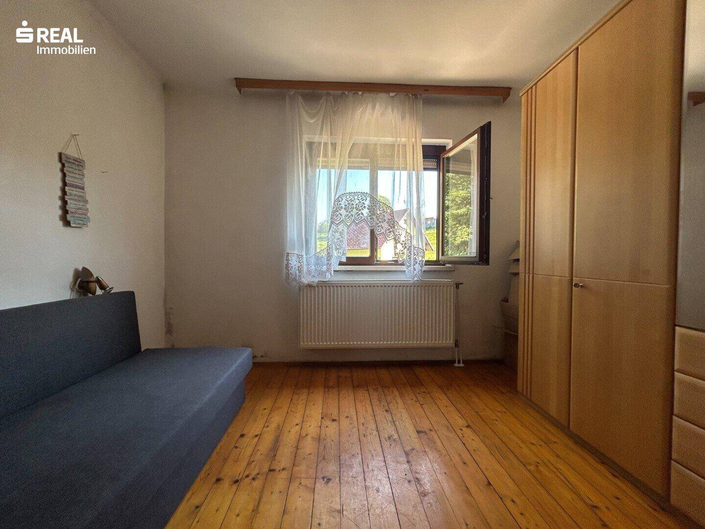 Schlafzimmer mit Holzdielenboden, Fenster und Kleiderschrank.