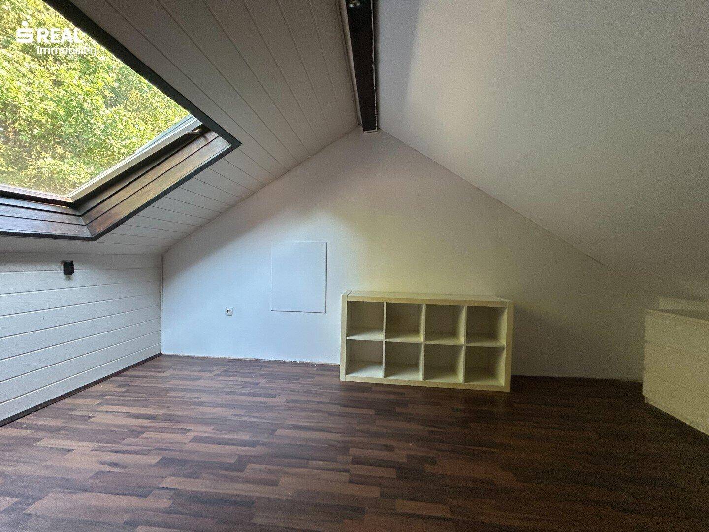 Heller Dachgeschossraum mit Dachfenster, Laminatboden und Stauraummöbeln.