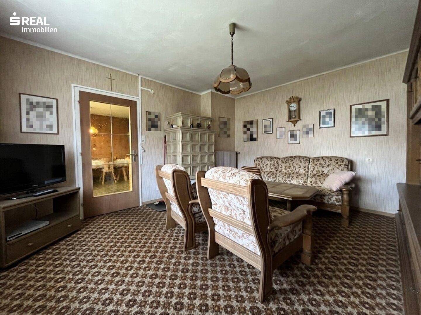 Gemütliches Wohnzimmer mit Teppichboden, Kachelofen und traditionellen Möbeln.