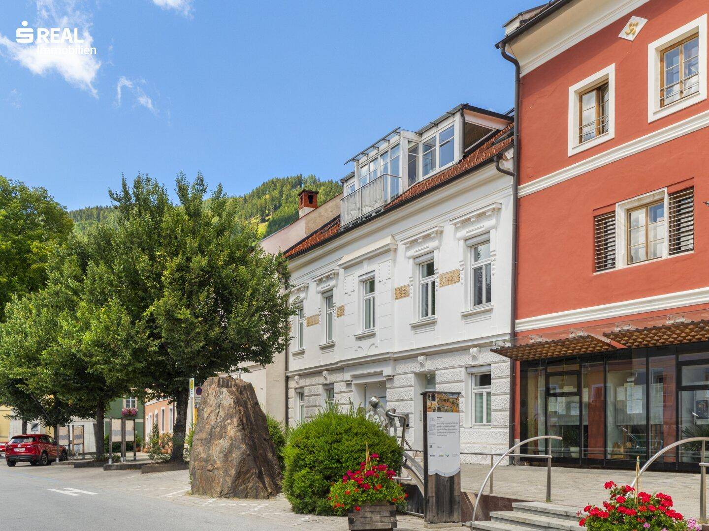 Ansicht der historischen Straßenfassade mit großen Fenstern und einem kleinen Balkon im Dachgeschoss.