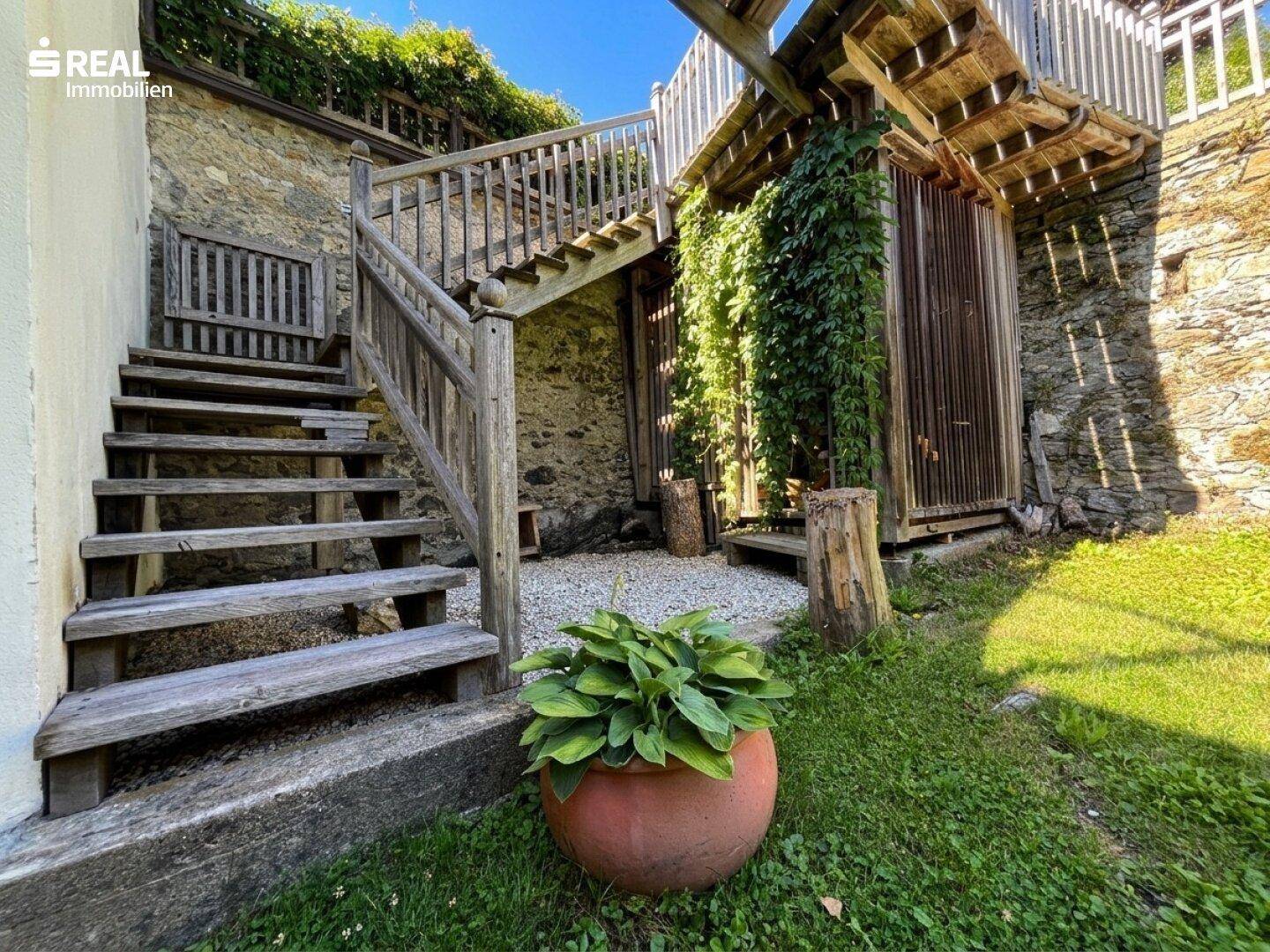 Rustikale Holztreppe im Gartenbereich, umgeben von üppigem Grün und einer Steinmauer.