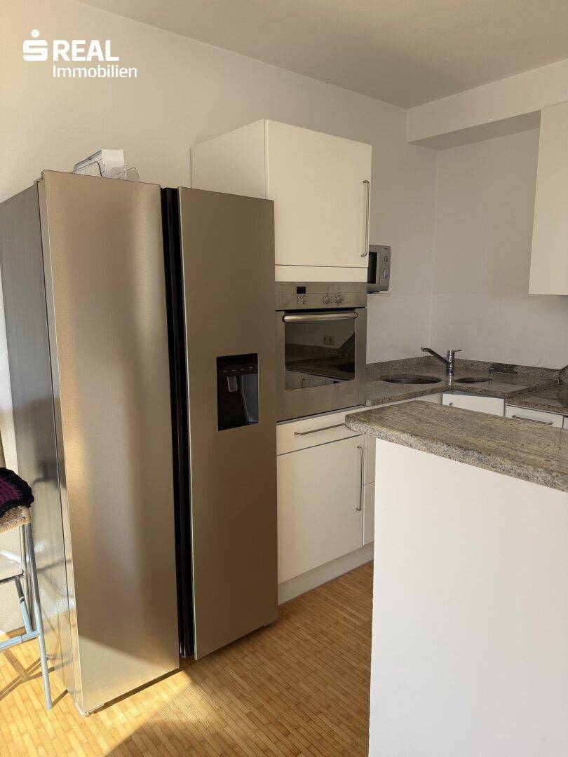 Moderne Küche mit großem Kühlschrank, Backofen und Arbeitsplatte aus Granit.