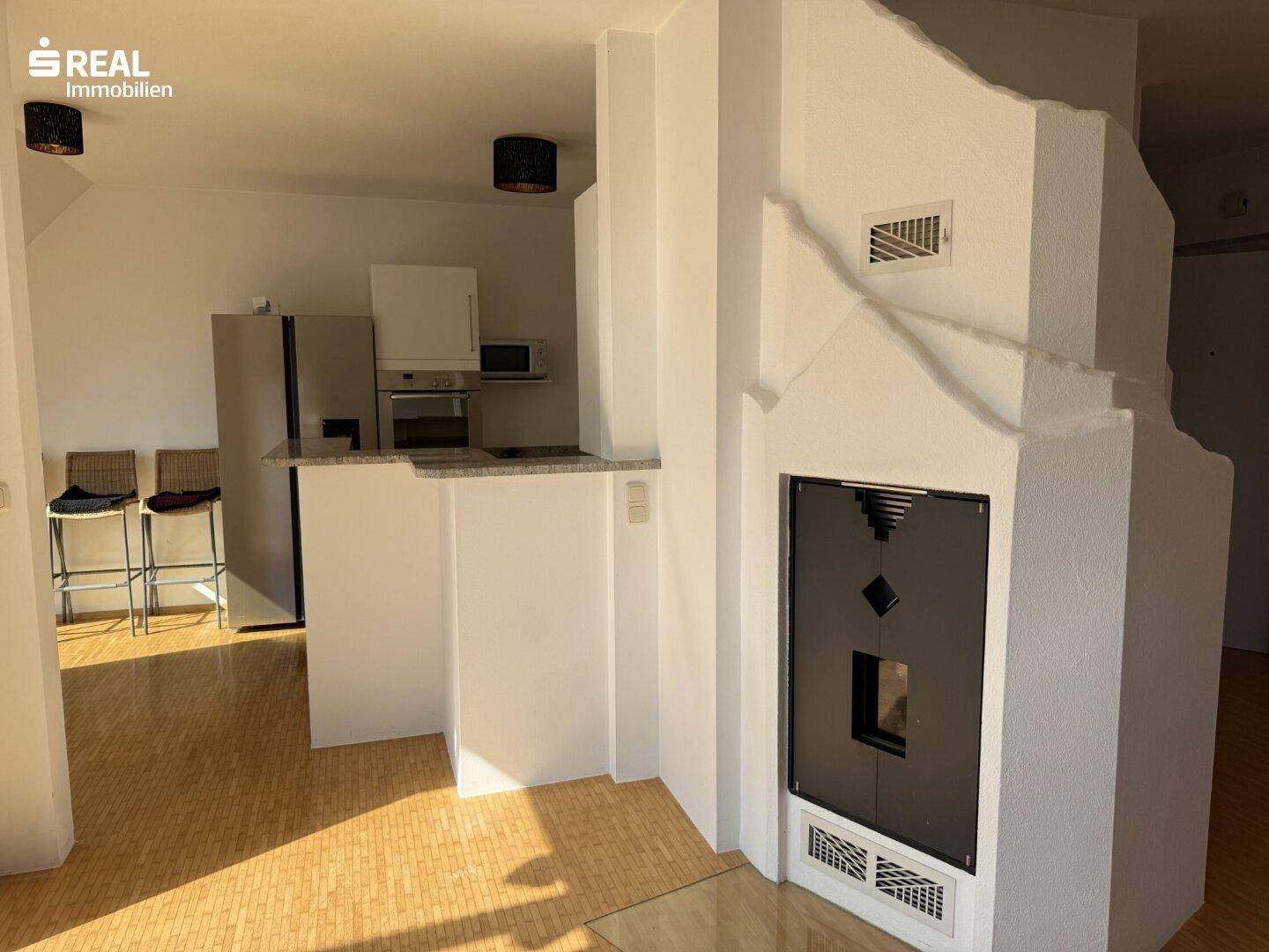 Offener Wohnbereich mit Kamin, Holzboden und Blick auf die angrenzende Küchenzeile.