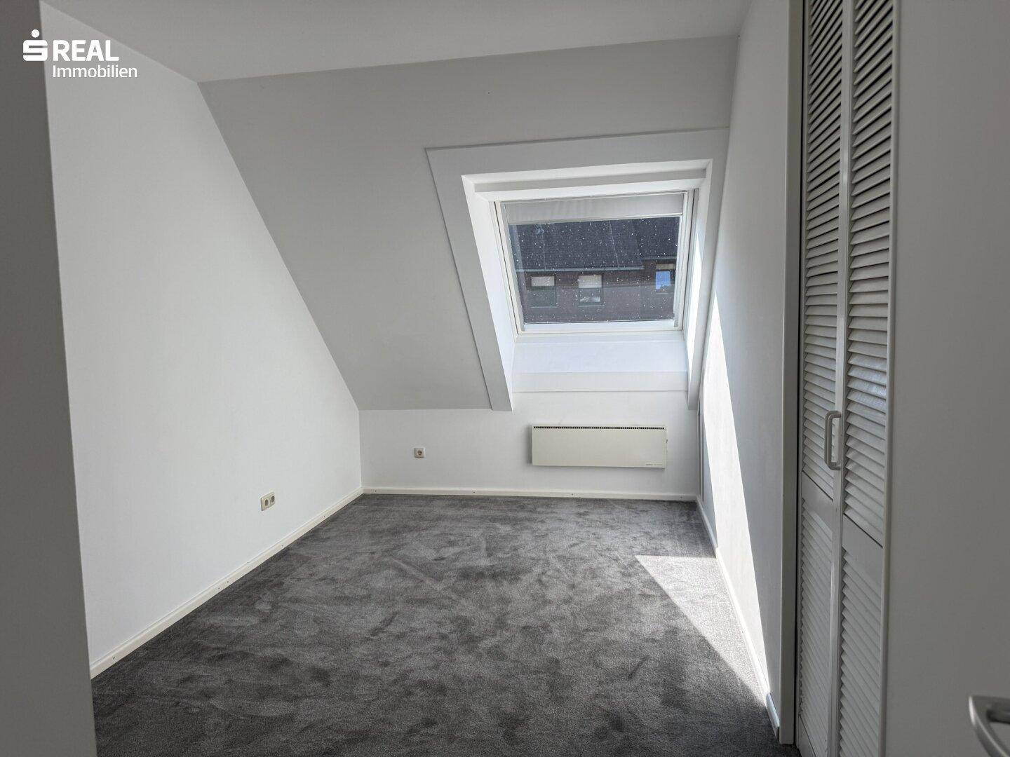 Schlafzimmer im Dachgeschoss mit Dachfenster, Teppichboden und schrägen Wänden.