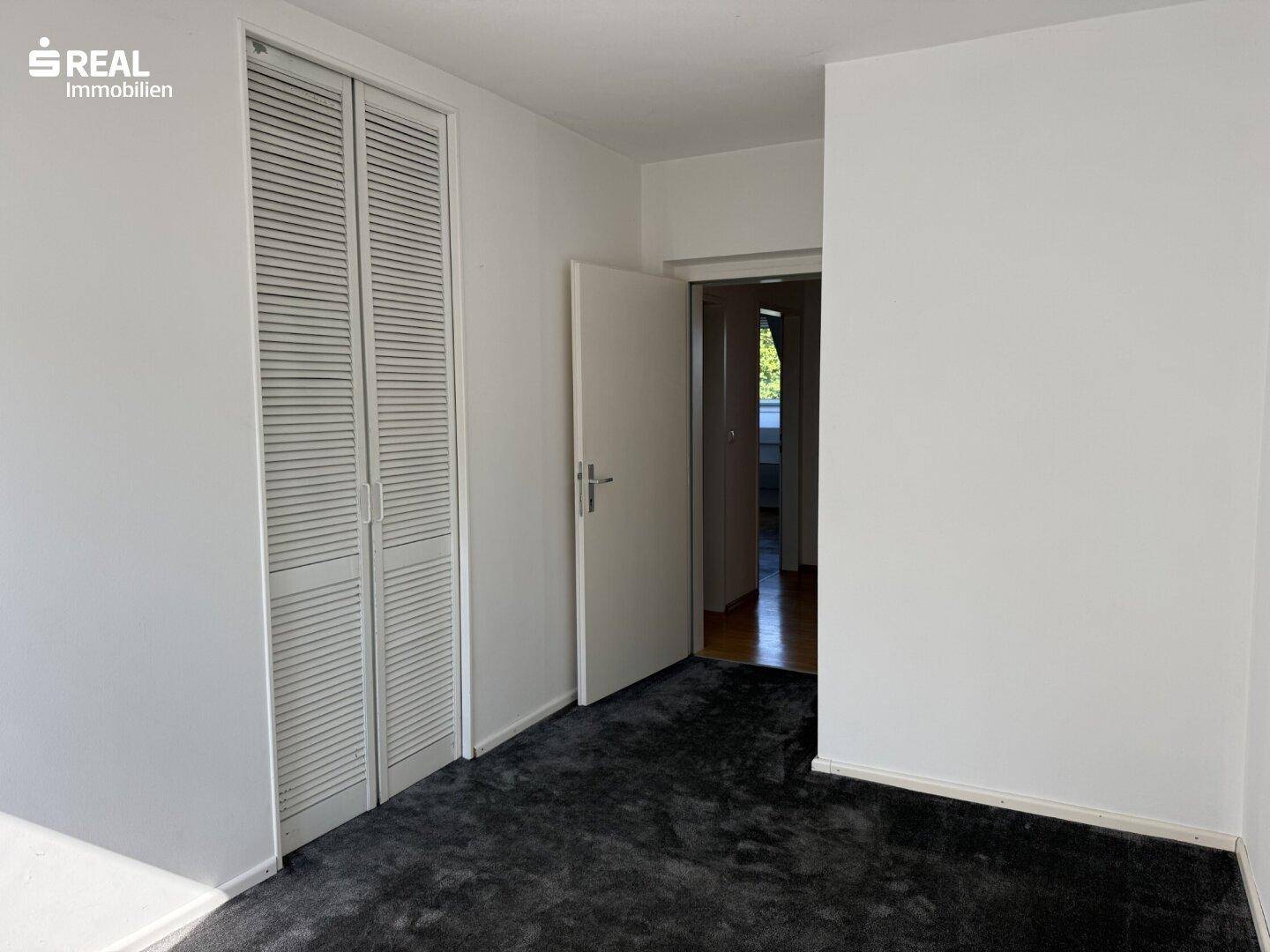 Schlafzimmer mit Teppichboden, weißen Wänden und integrierten Schranktüren.