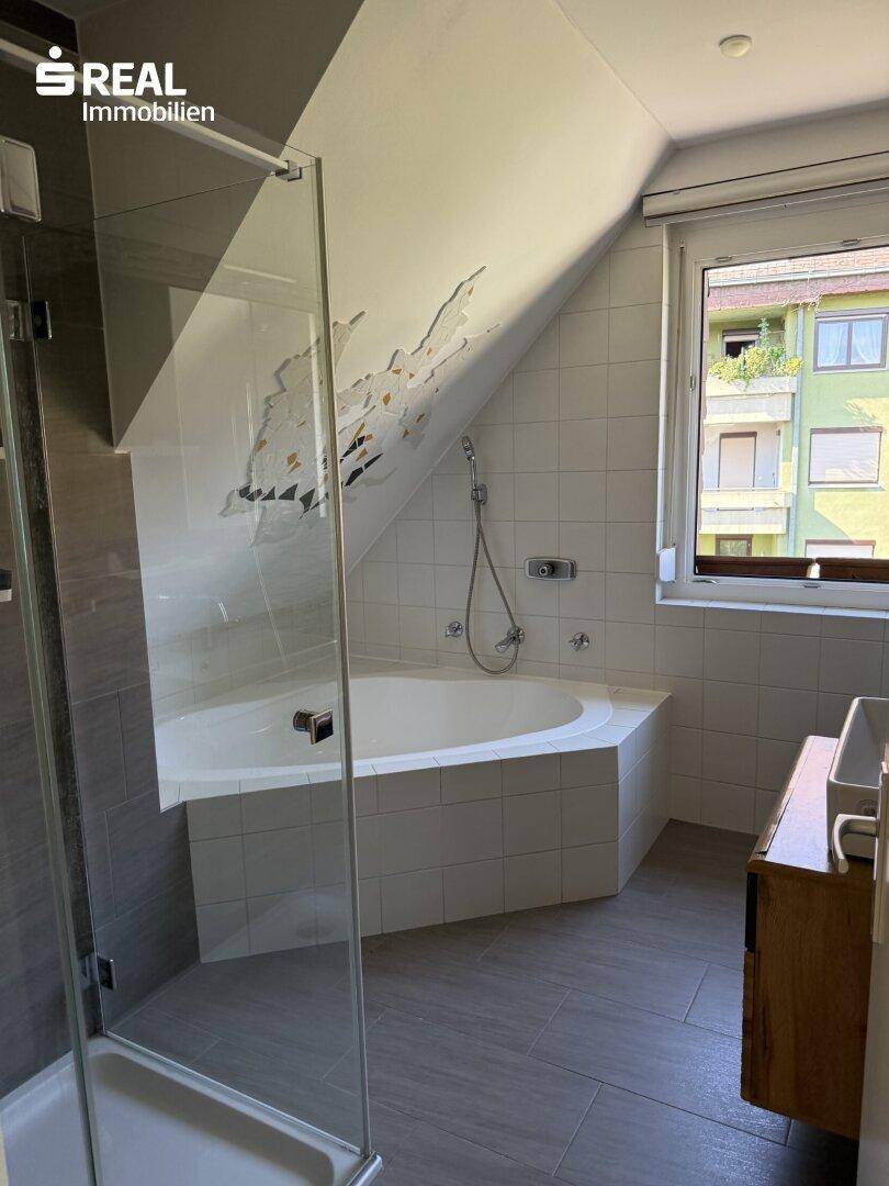 Badezimmer im Dachgeschoss mit Badewanne, Dusche und Fenster für natürliche Belüftung.