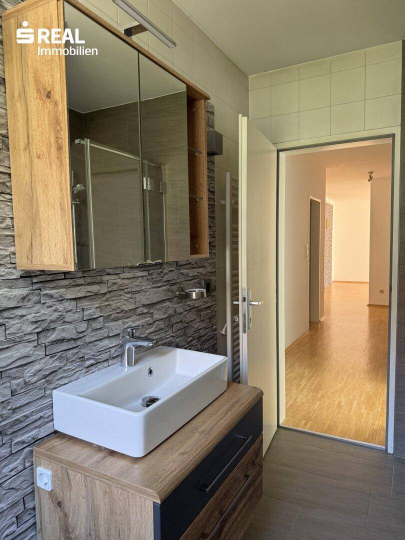 Modernes Badezimmer mit Aufsatzwaschbecken, Spiegelschrank und Steinwand-Akzenten.