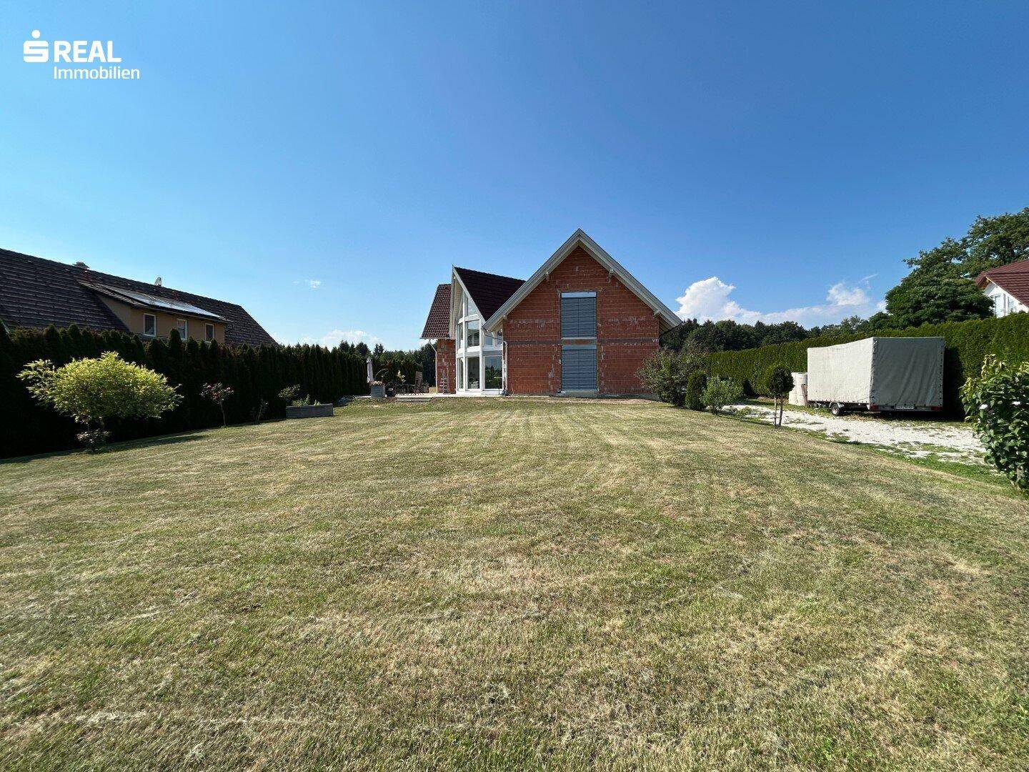 Weitläufiger Gartenbereich mit großer Rasenfläche und Blick auf das Einfamilienhaus im Hintergrund.