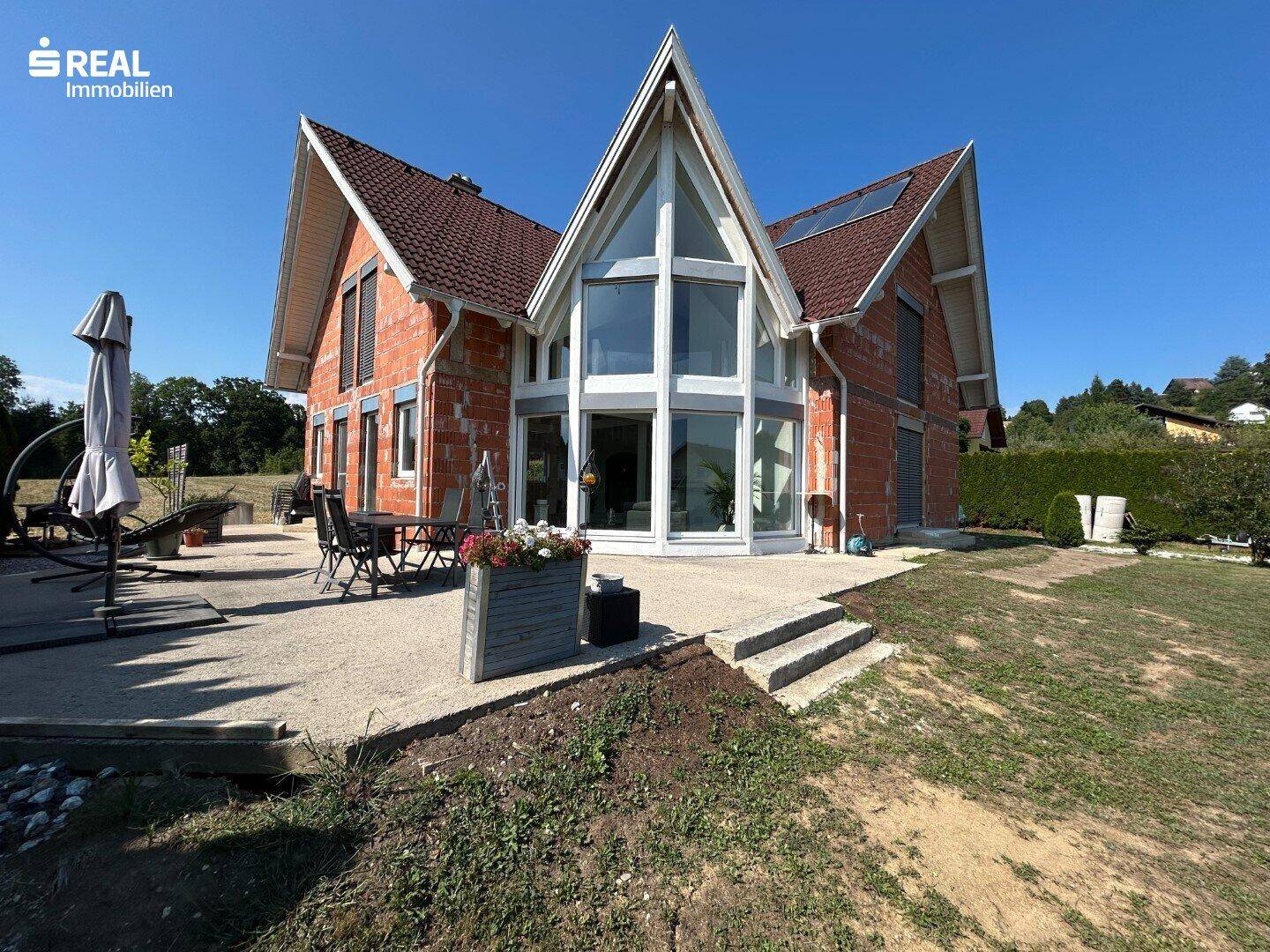 Außenansicht eines Neubaus mit großer Glasfassade, Terrasse und weitläufigem Gartenbereich.
