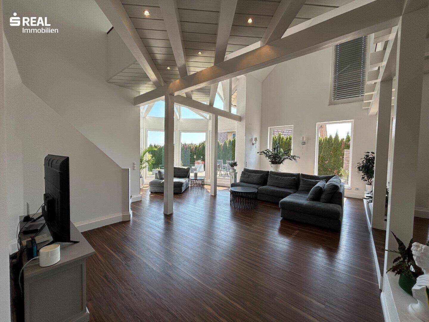 Geräumiges Wohnzimmer mit dunklem Holzboden, hohen Decken und Zugang zum Außenbereich.