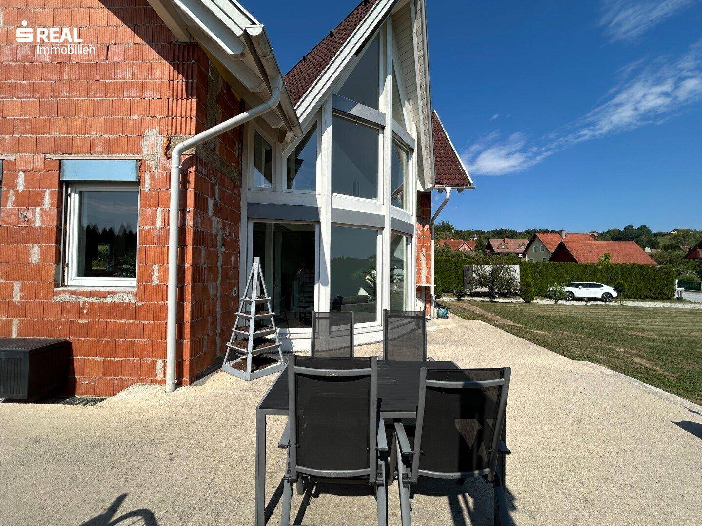 Detailansicht der Terrasse mit Gartenmöbeln und der beeindruckenden Glasfront des Hauses.