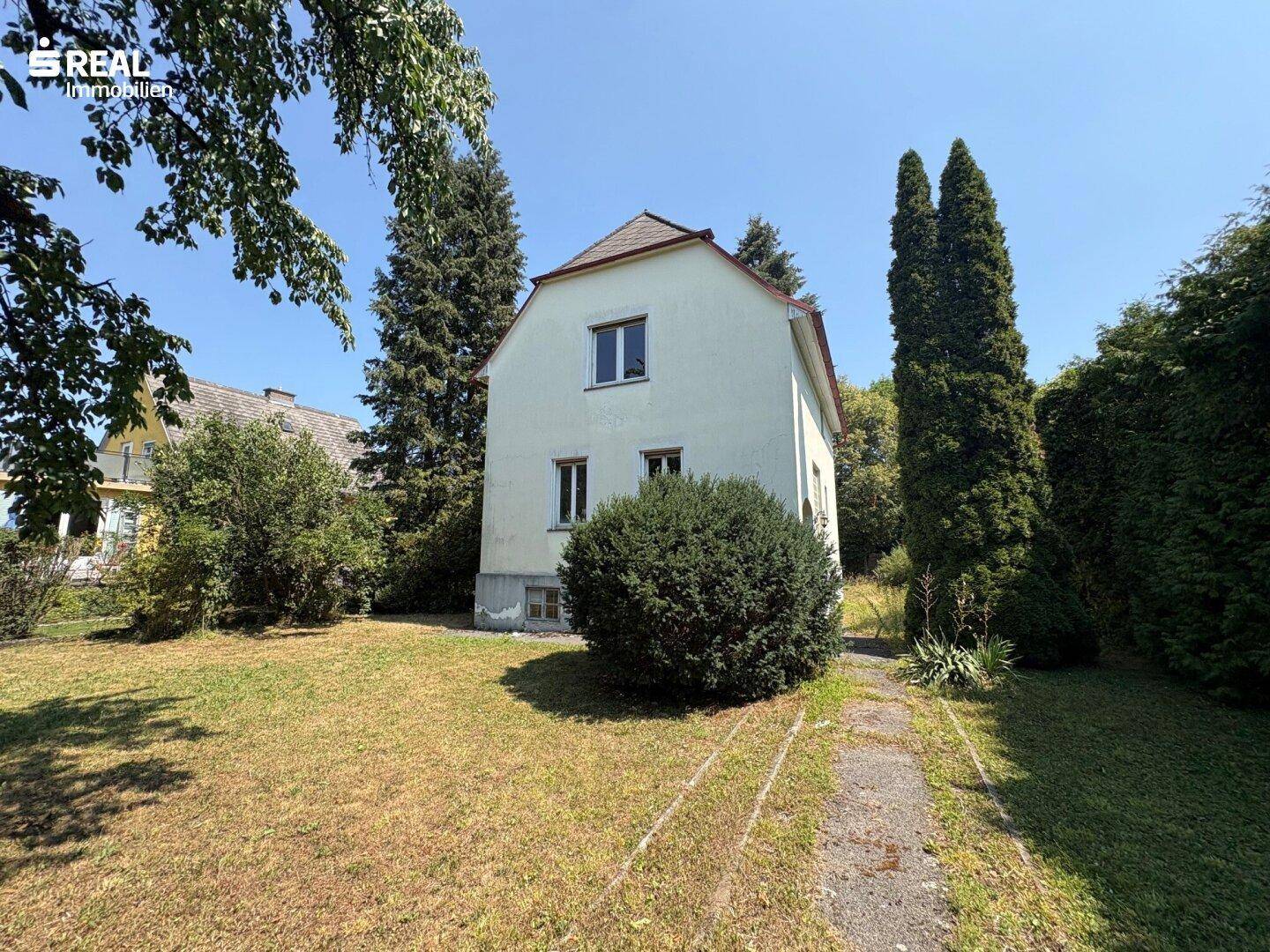 Klassisches Einfamilienhaus mit weißer Fassade und gepflegtem Vorgarten unter blauem Himmel.