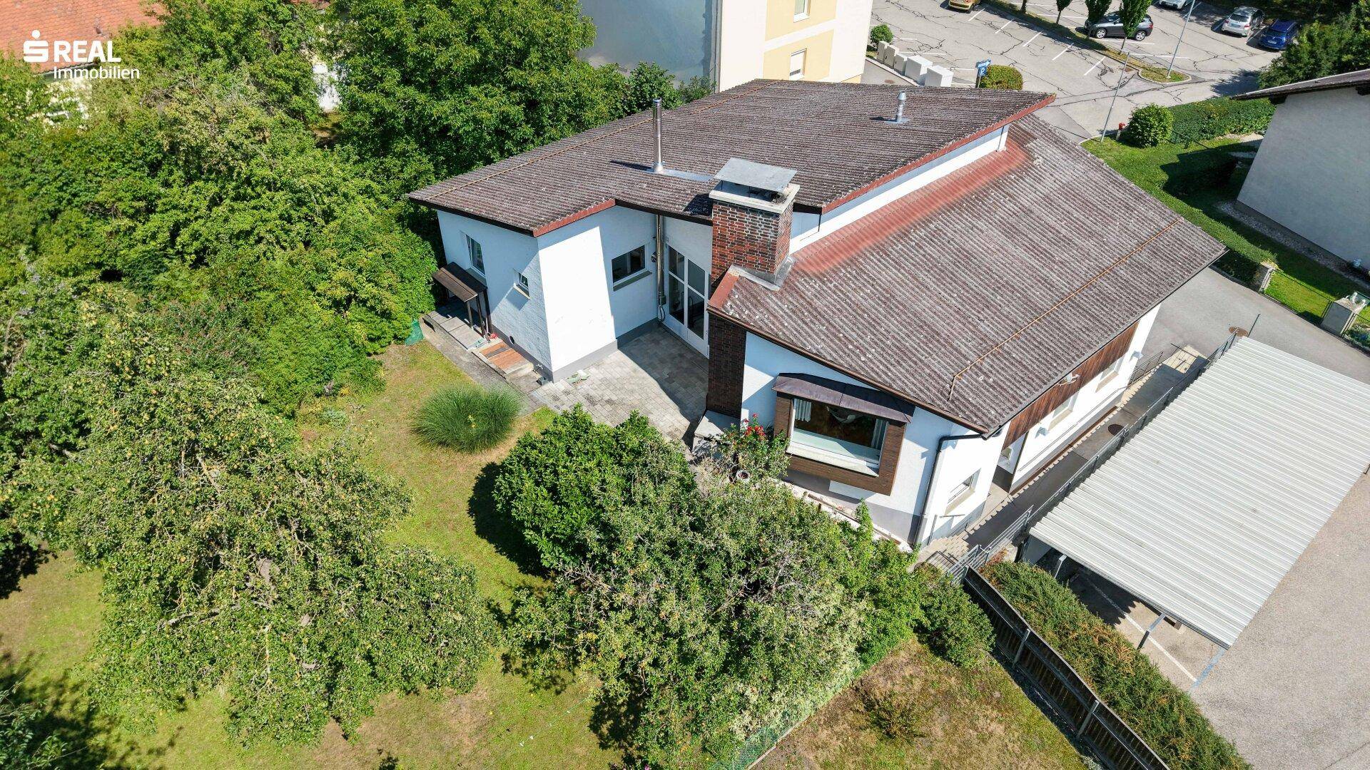 Vogelperspektive des Hauses mit weitläufigem Gartenbereich und Carport unter strahlendem Himmel.
