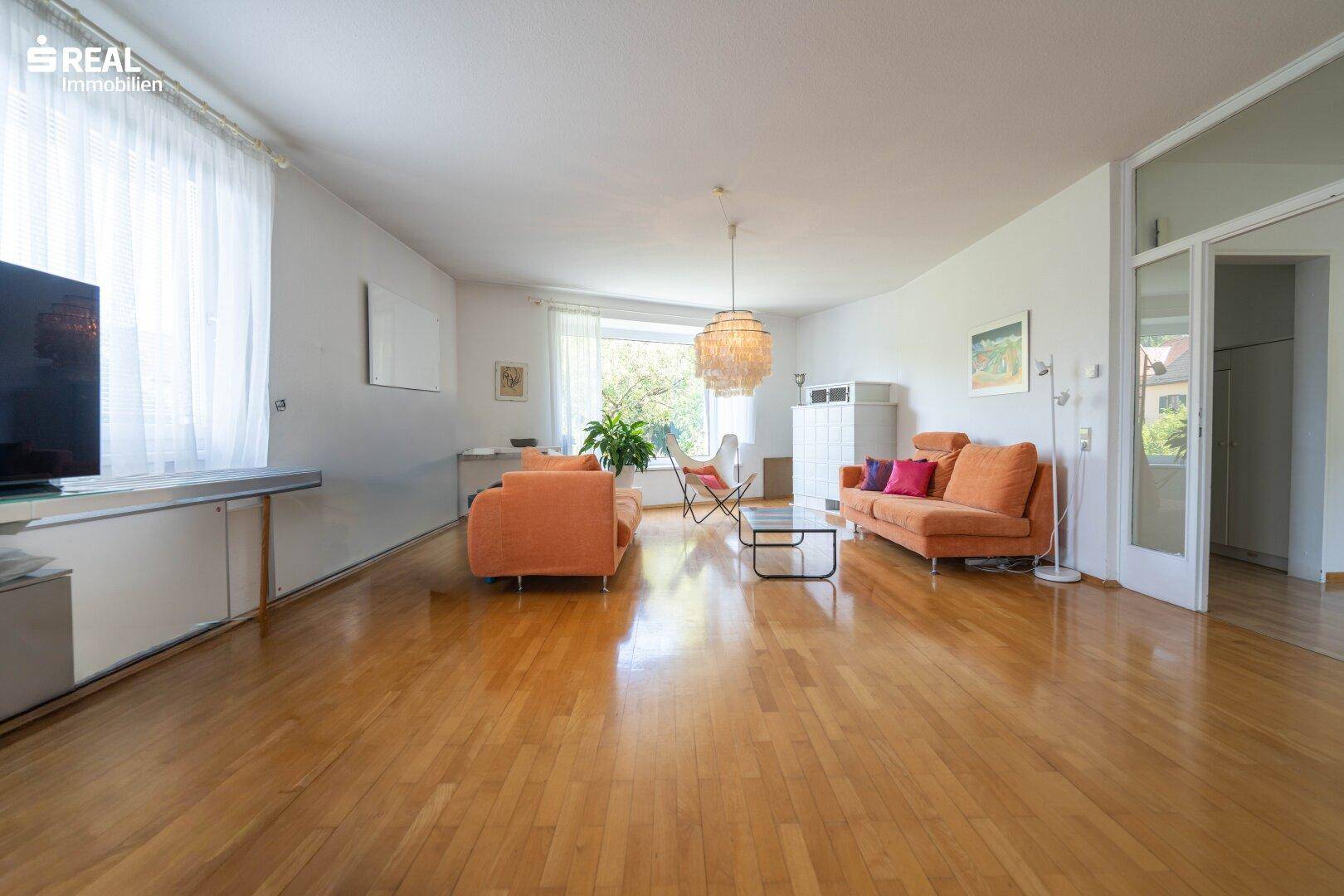 Helles Wohnzimmer mit Holzparkett, modernen Sofas und großem Fenster mit Blick ins Grüne.