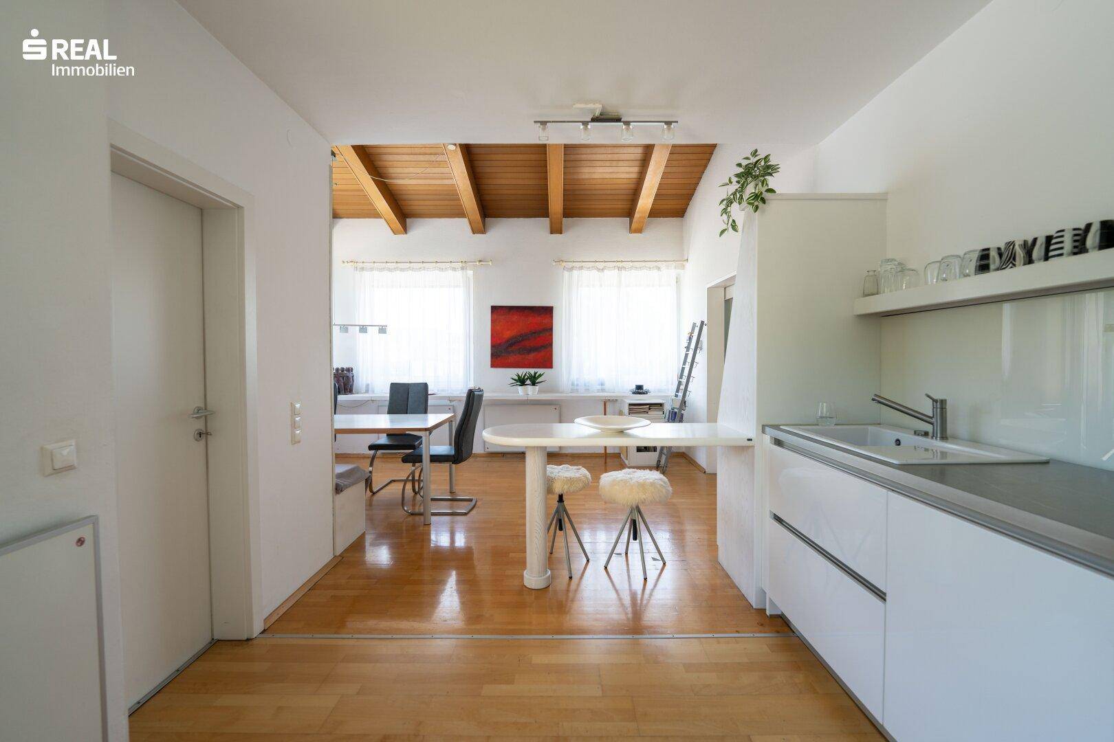 Moderne Küche mit weißen Schränken, Holzboden und offener Verbindung zum Essbereich.