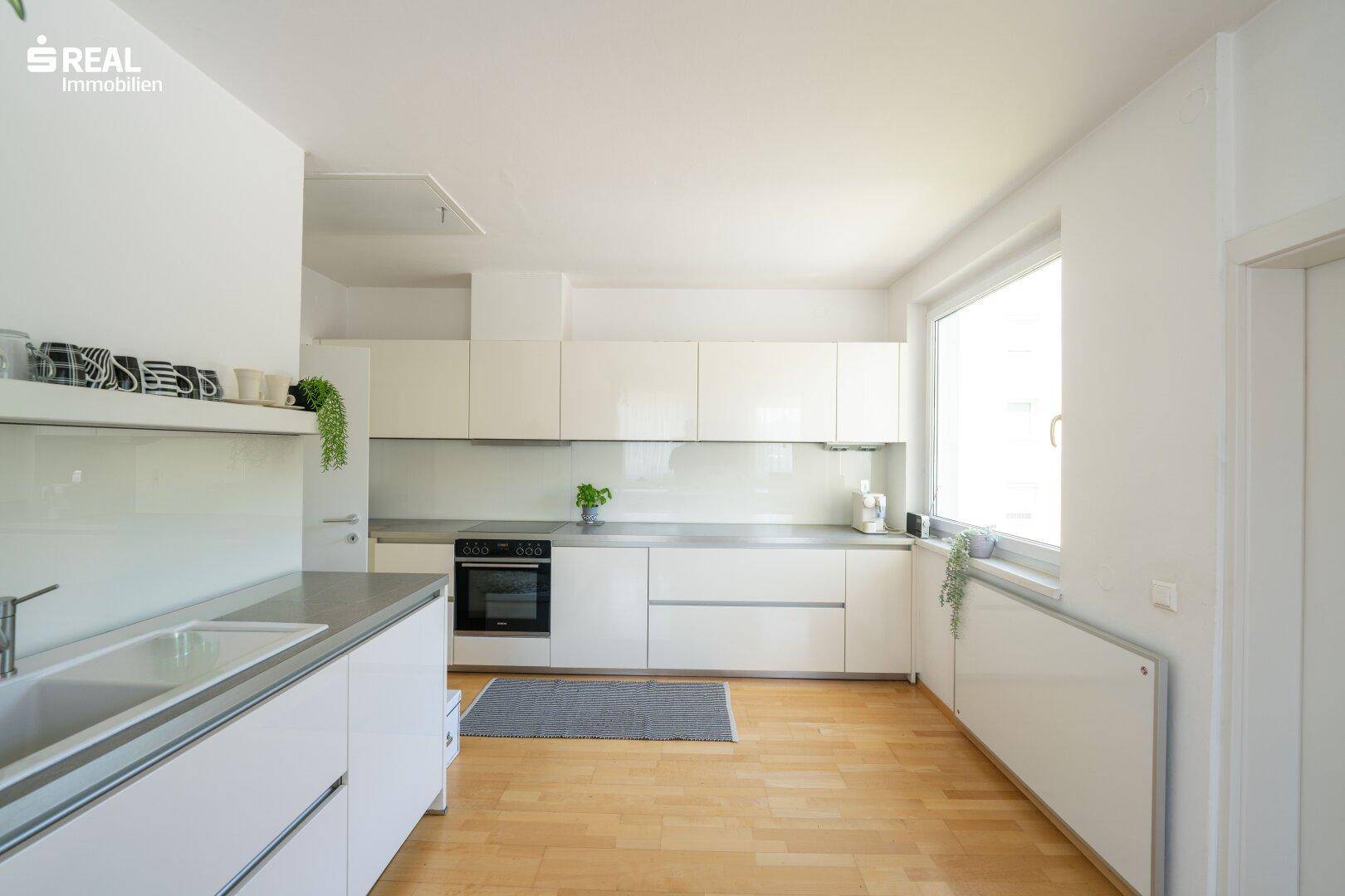 Moderne Einbauküche mit weißen Hochglanzfronten, integriertem Backofen und Fenster.