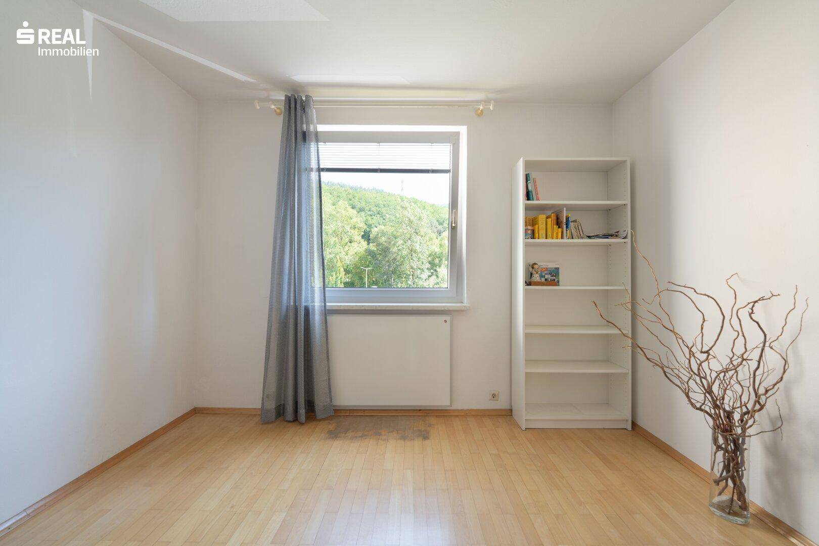 Helles Schlafzimmer oder Kinderzimmer mit Fenster und Blick ins Grüne, ausgestattet mit einem Regal.