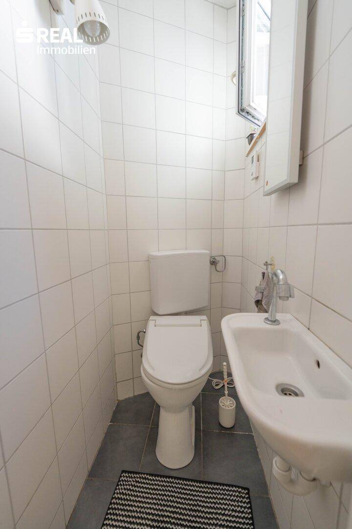 Kleines Gäste-WC mit Fenster, WC und Waschbecken, komplett gefliest in Weiß.