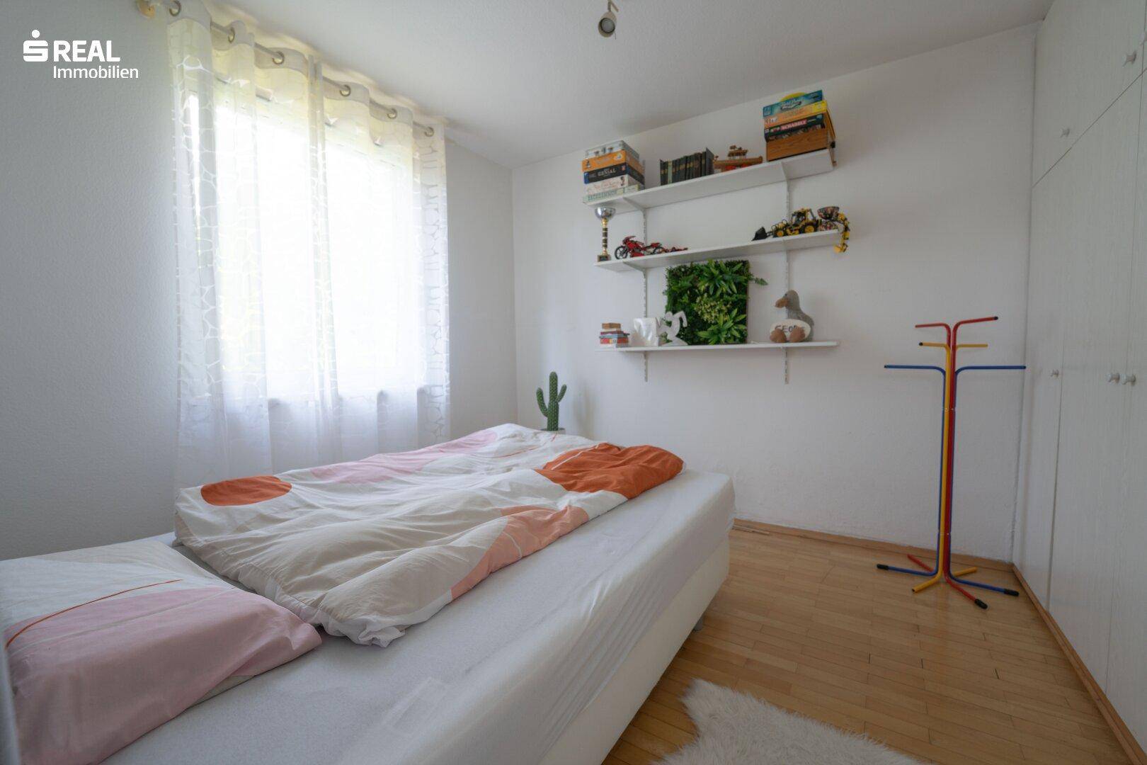Kinderzimmer mit Bett, Regalen und Fenster, hell und funktional eingerichtet.