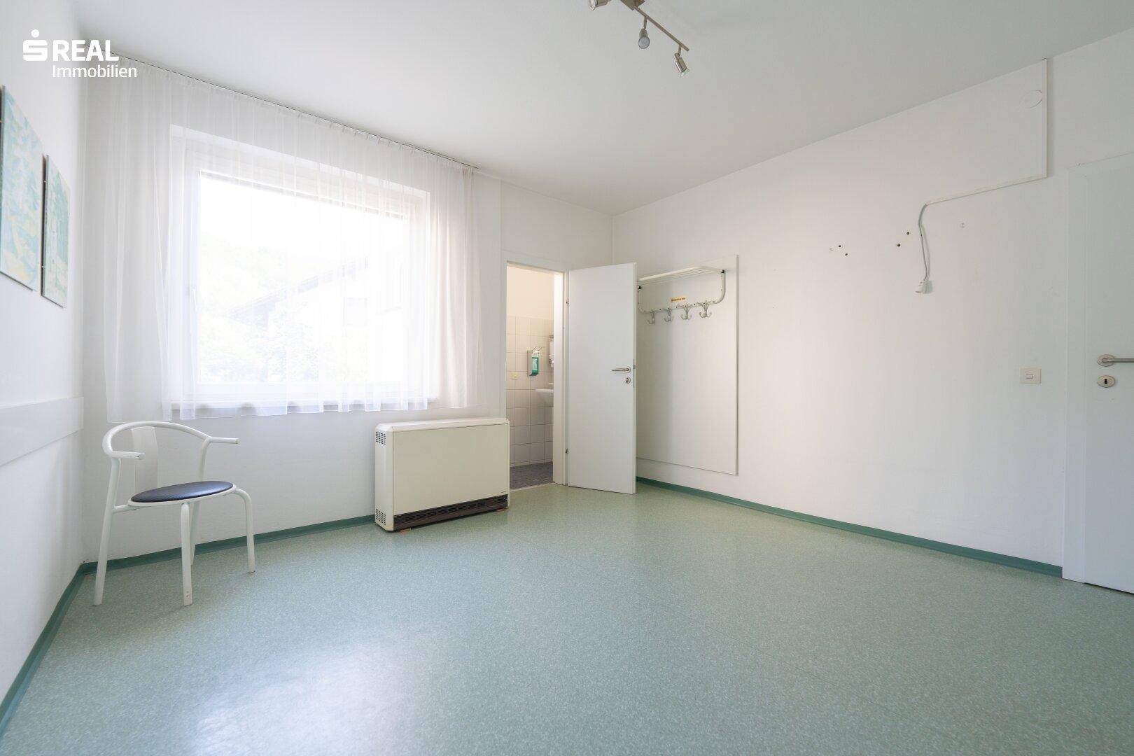 Heller Raum mit großem Fenster, Heizkörper und Zugang zu einem weiteren Zimmer.
