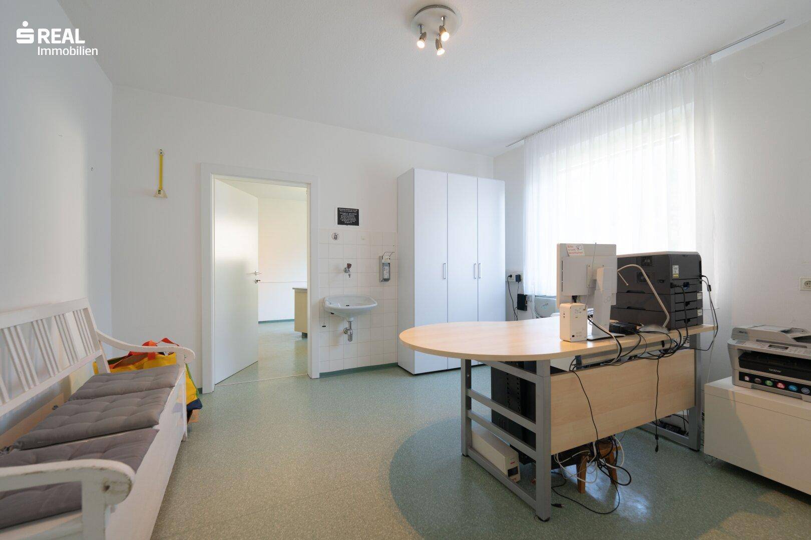 Vielseitiger Büroraum mit Schreibtisch, Sitzbank, Schränken und einem praktischen Waschbecken.