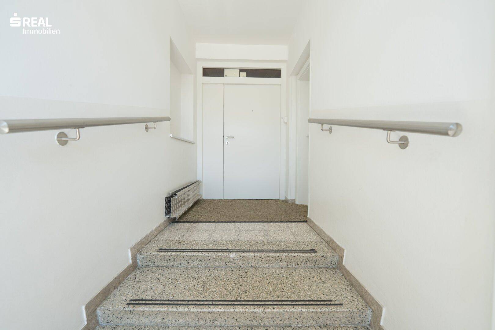 Eingangsbereich mit Treppe und Handläufen, führt zur Wohnungstür.