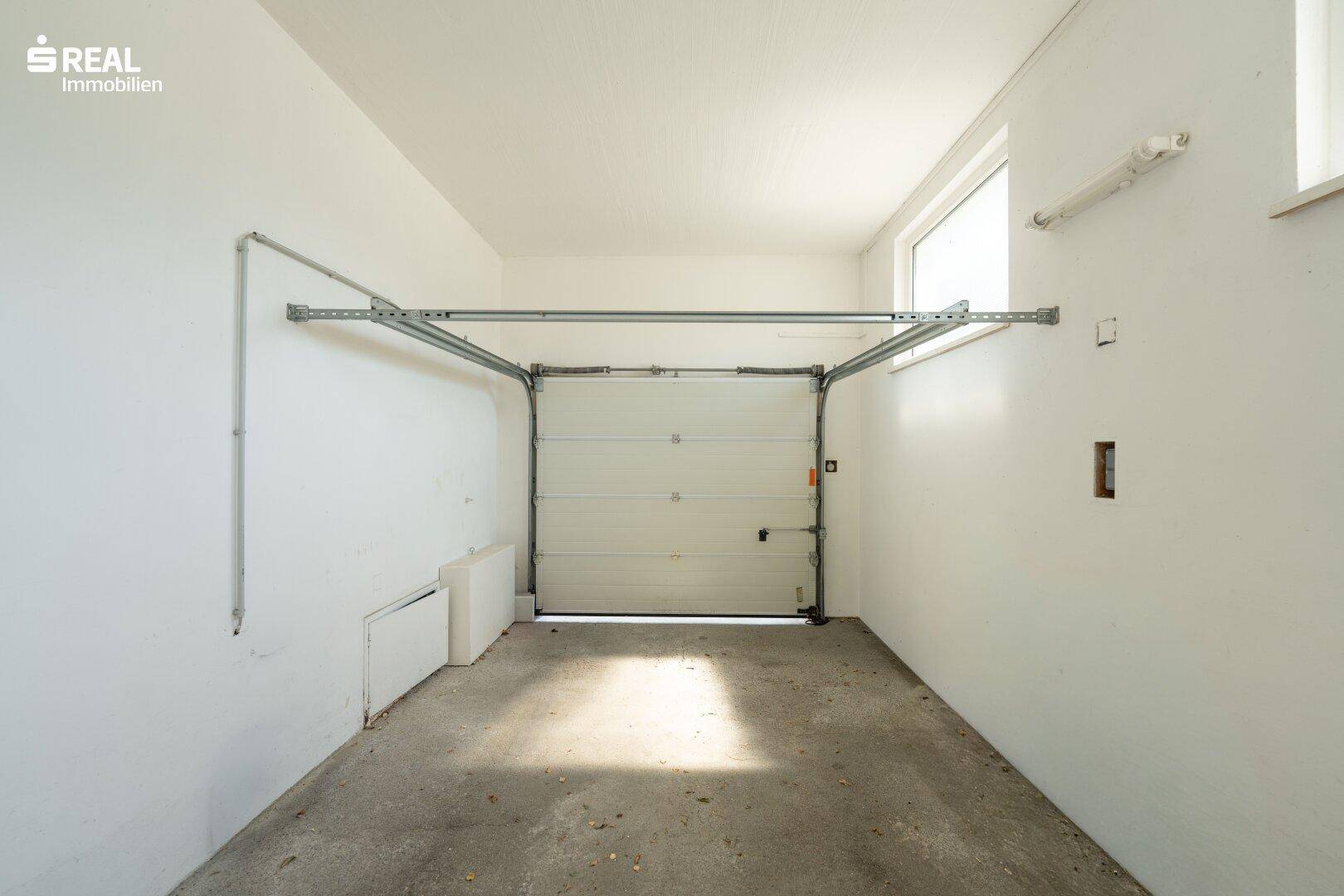 Leere Garage mit Rolltor, Betonboden und einem Fenster für Tageslicht.