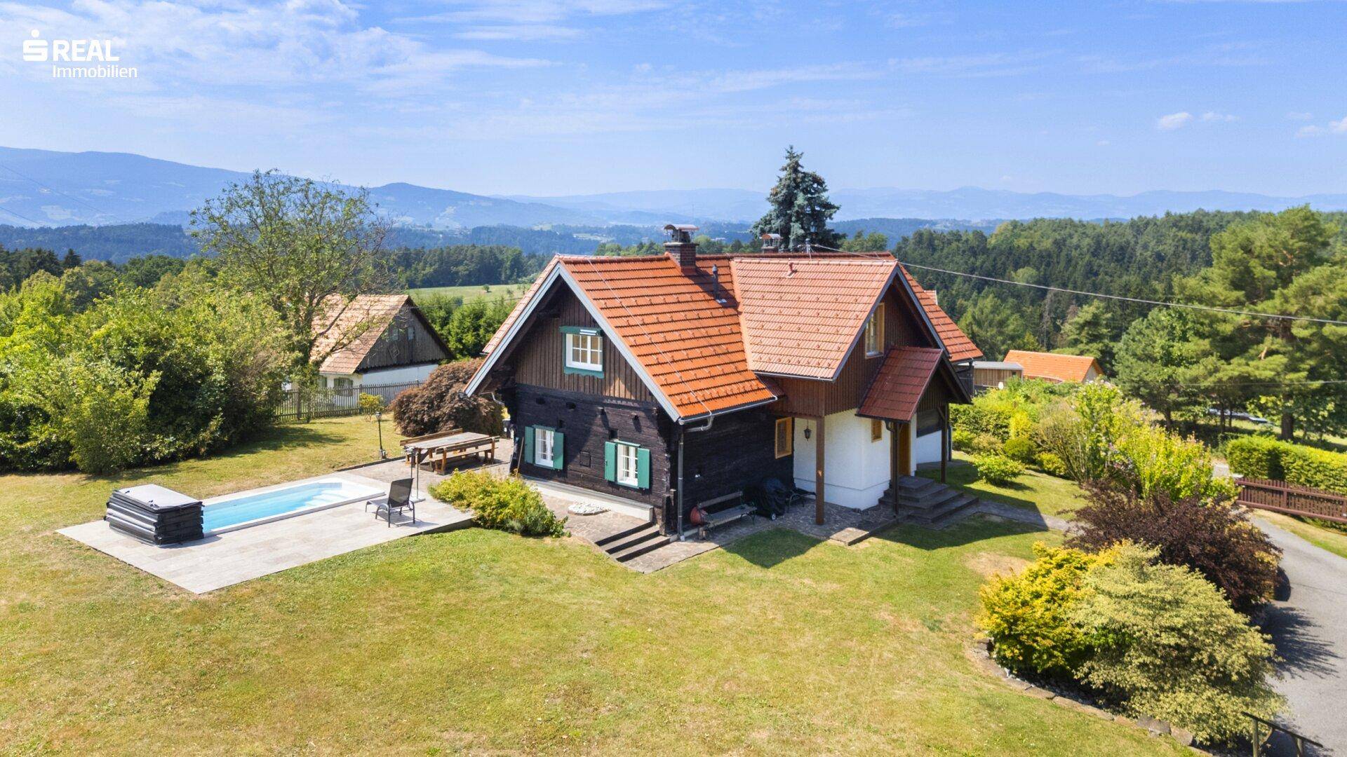 Idyllisches Landhaus mit Pool und weitläufigem Garten, umgeben von grüner Natur und Bergen.