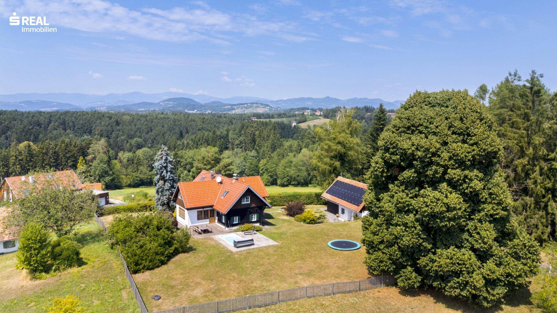 Weitläufiges Grundstück mit zwei Gebäuden, Pool und Trampolin, eingebettet in eine grüne Hügellandschaft.