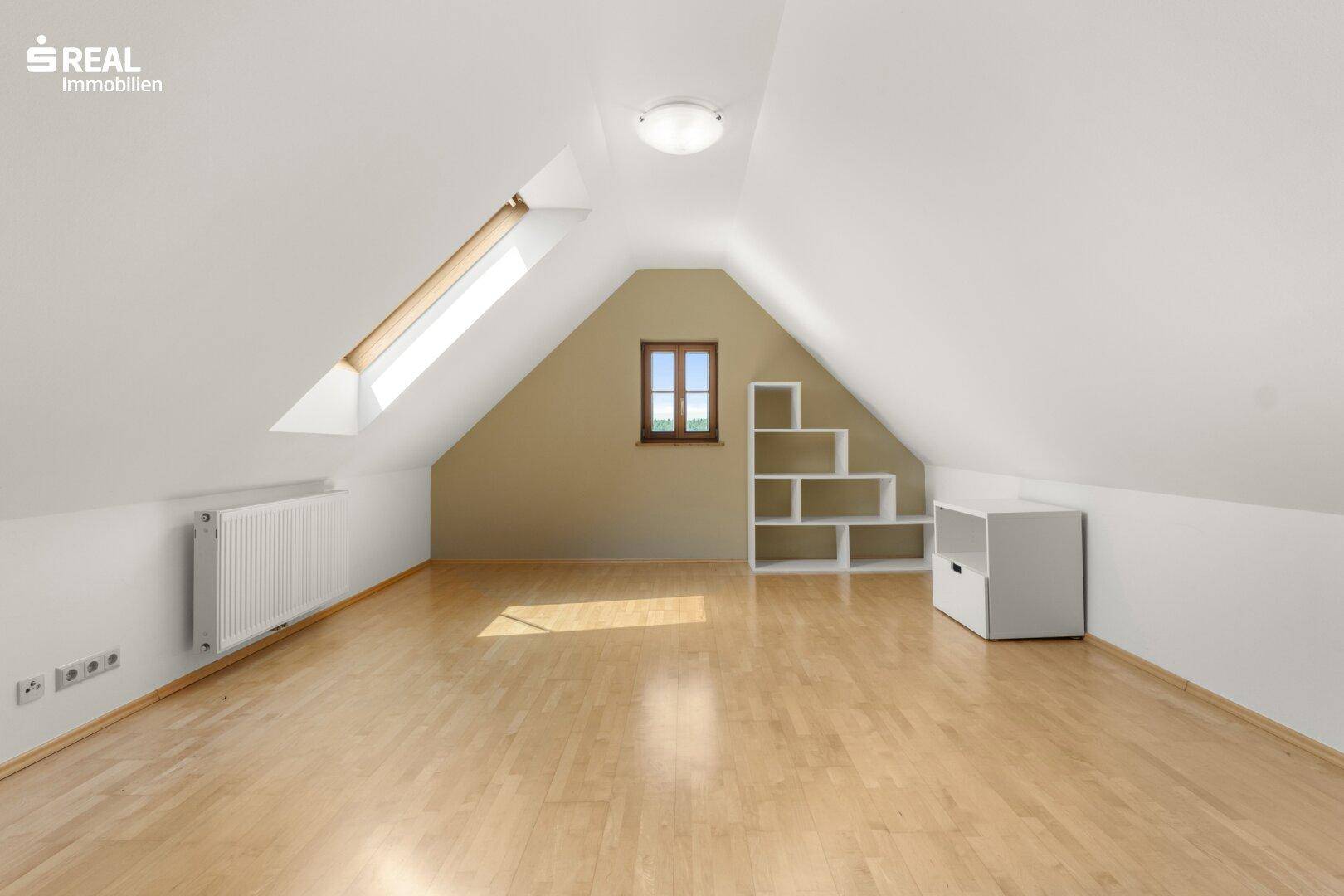 Ausgebauter Dachbodenraum mit Holzboden, Dachschrägen und einem Dachfenster für natürliches Licht.