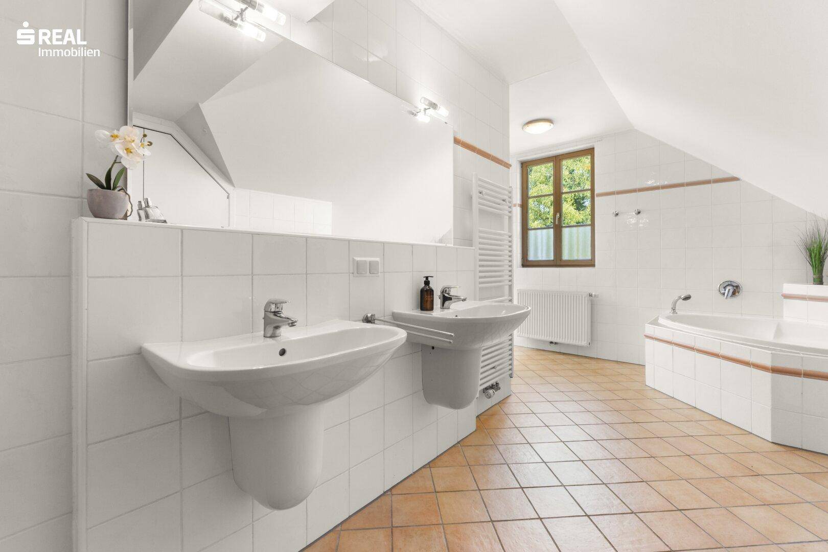 Geräumiges Badezimmer mit Doppelwaschbecken, Badewanne und Terrakotta-Fliesenboden im Dachgeschoss.