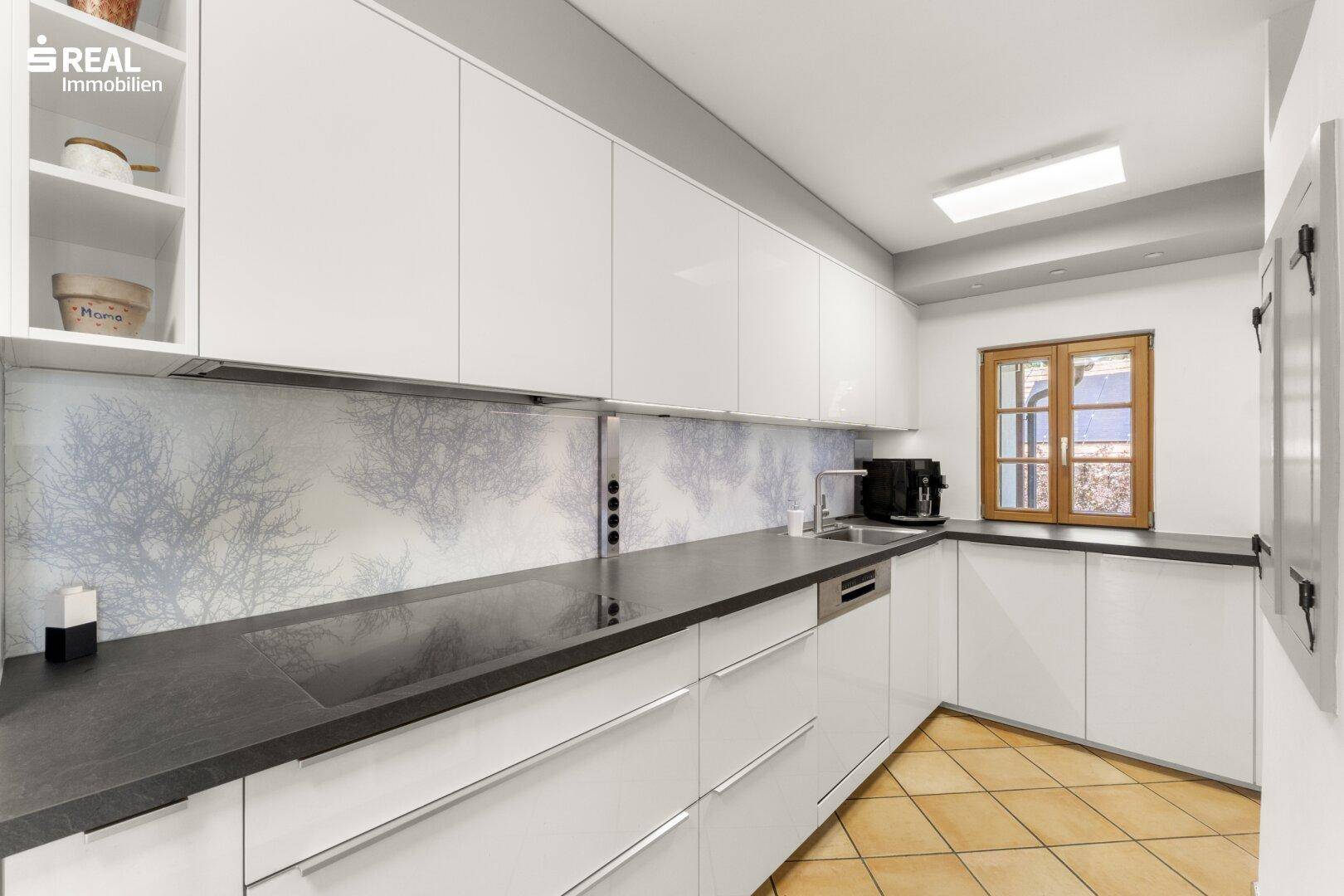 Moderne Küche mit weißen Hochglanzfronten, dunkler Arbeitsplatte und Terrakotta-Fliesenboden.