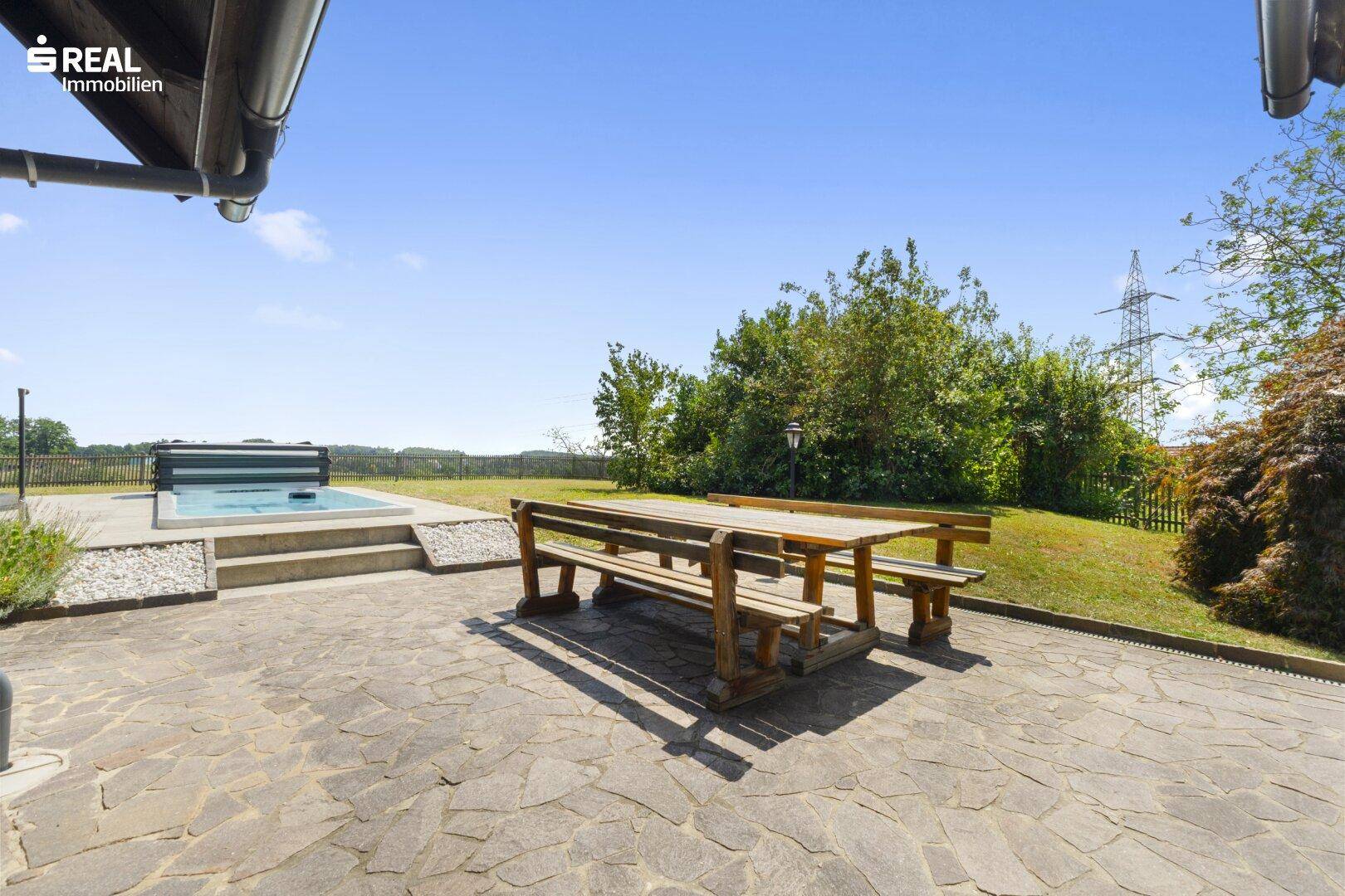 Große Steinterrasse mit Holztischgarnitur und Blick auf den Pool und die umliegende Landschaft.