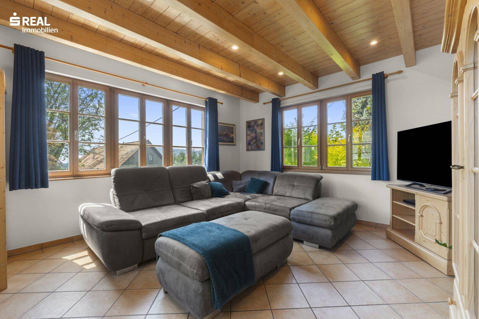 Rustikales Wohnzimmer mit Holzbalkendecke, großem Ecksofa und Fliesenboden.