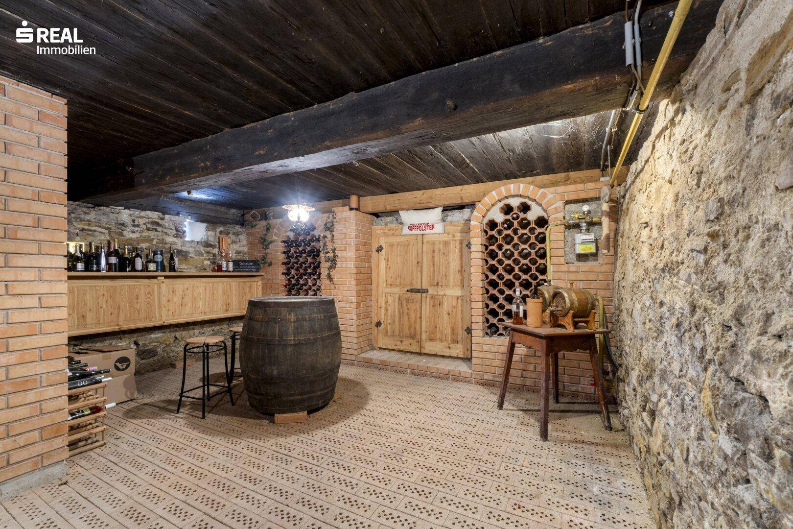 Rustikaler Weinkeller mit Ziegelwänden, Holzbalkendecke und zahlreichen Weinregalen.