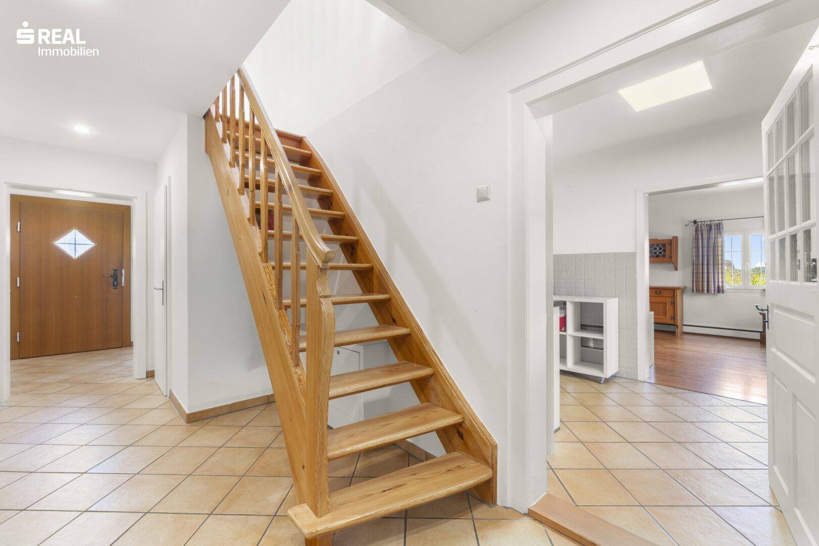 Heller Eingangsbereich mit Holztreppe und Terrakotta-Fliesenboden, der zu den oberen Etagen führt.
