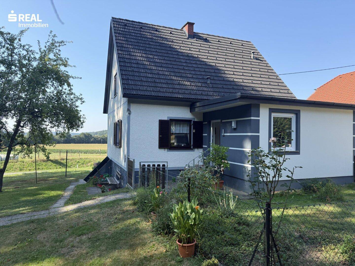 Seitenansicht des Hauses mit gepflegtem Gartenbereich und Blick auf die Felder.